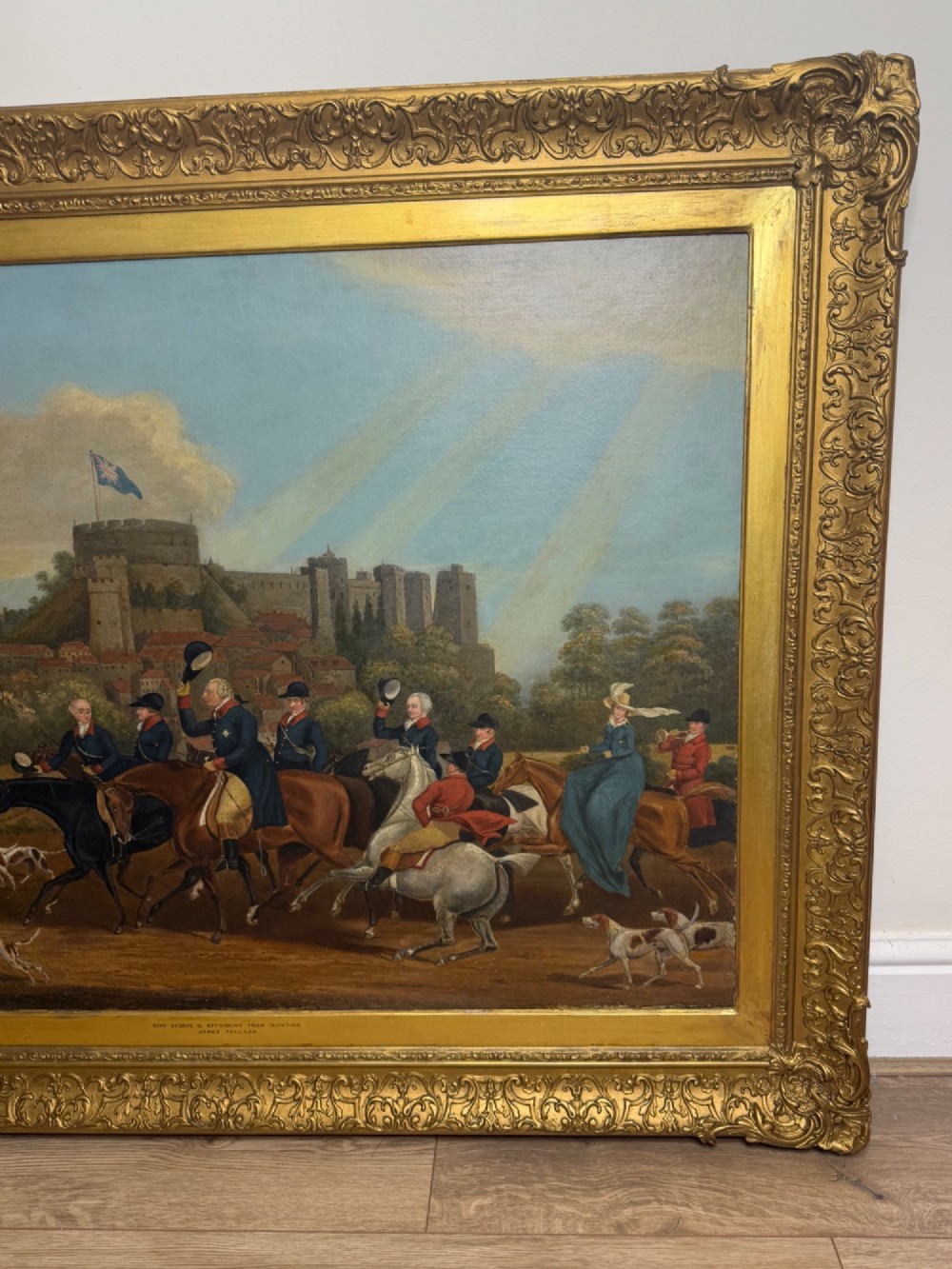 An antique oil painting on canvas depicting King George and hunters on horseback with hounds before Windsor Castle, housed in an ornate carved gilt frame. View V