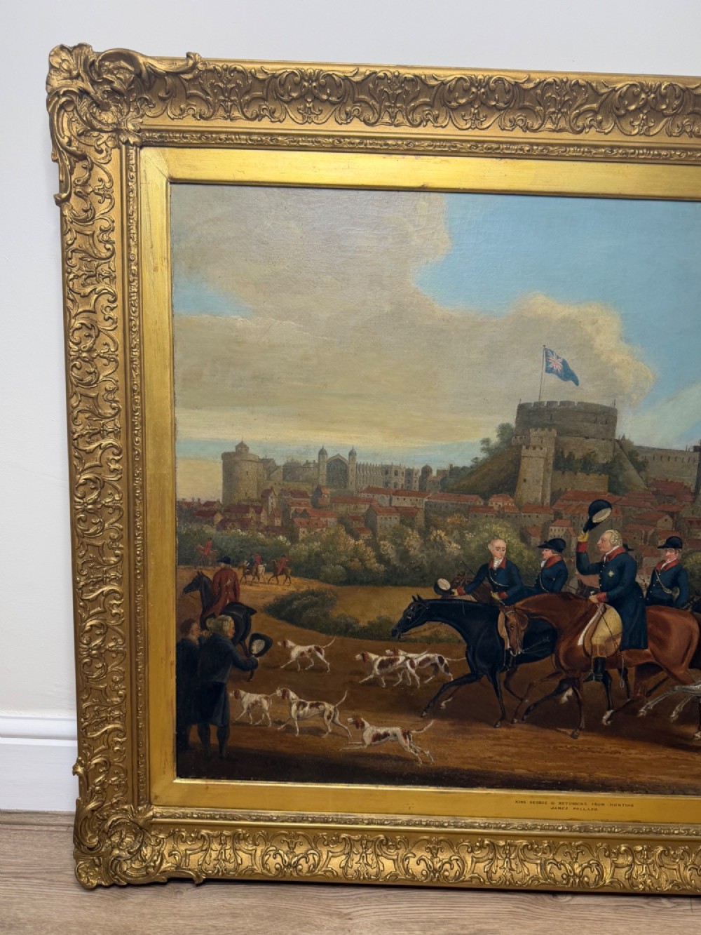 An antique oil painting on canvas depicting King George and hunters on horseback with hounds before Windsor Castle, housed in an ornate carved gilt frame. View VI