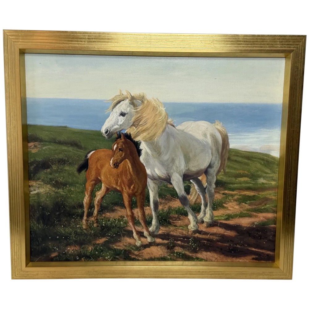 A framed oil painting featuring a grey mare standing beside a young chestnut foal on a grassy coastal headland overlooking the sea.