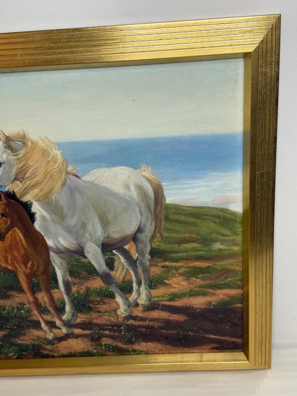 A framed oil painting featuring a grey mare standing beside a young chestnut foal on a grassy coastal headland overlooking the sea. View IV
