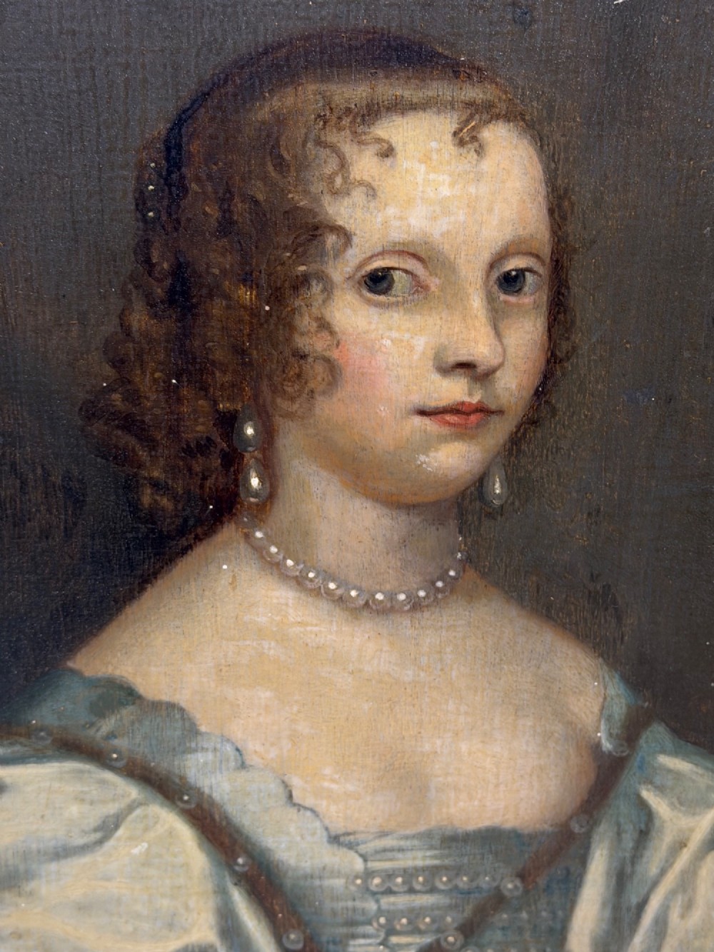 A 17th-century oil portrait painting on an oak panel depicting a woman with dark ringlets and pearl jewellery in a gadrooned gold leaf frame. View II
