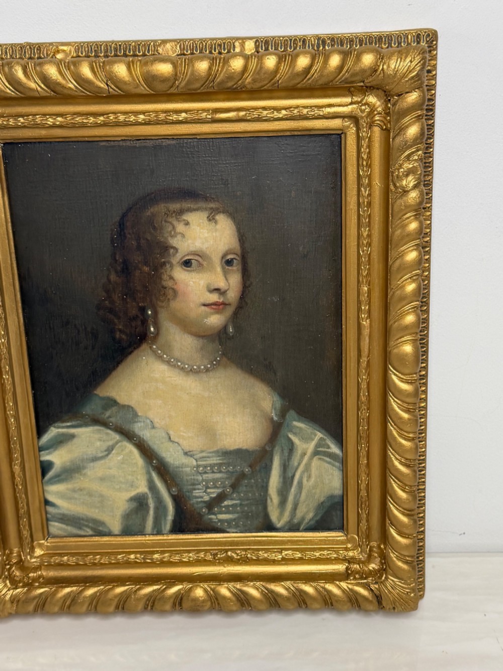 A 17th-century oil portrait painting on an oak panel depicting a woman with dark ringlets and pearl jewellery in a gadrooned gold leaf frame. View IV