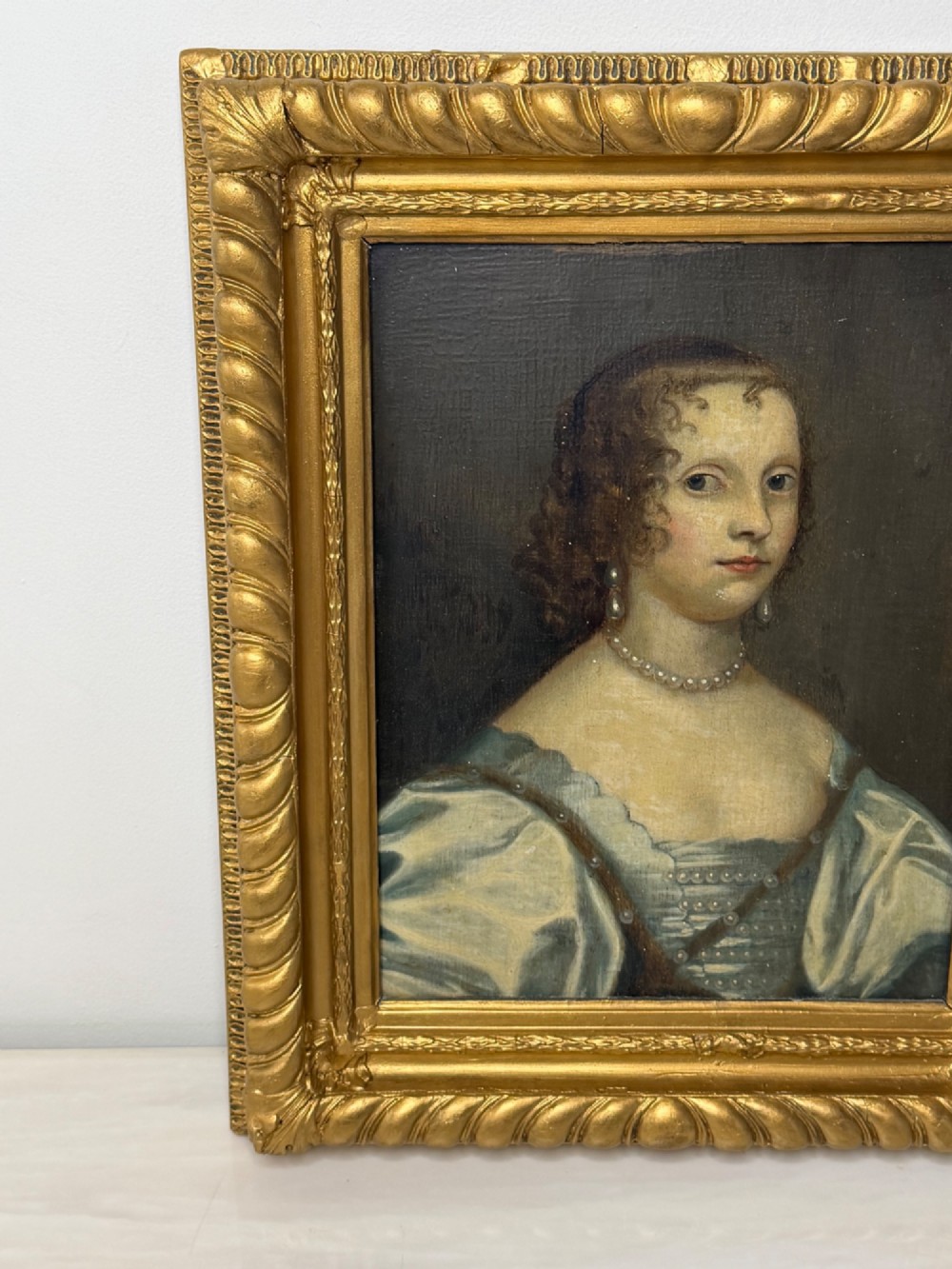 A 17th-century oil portrait painting on an oak panel depicting a woman with dark ringlets and pearl jewellery in a gadrooned gold leaf frame. View V