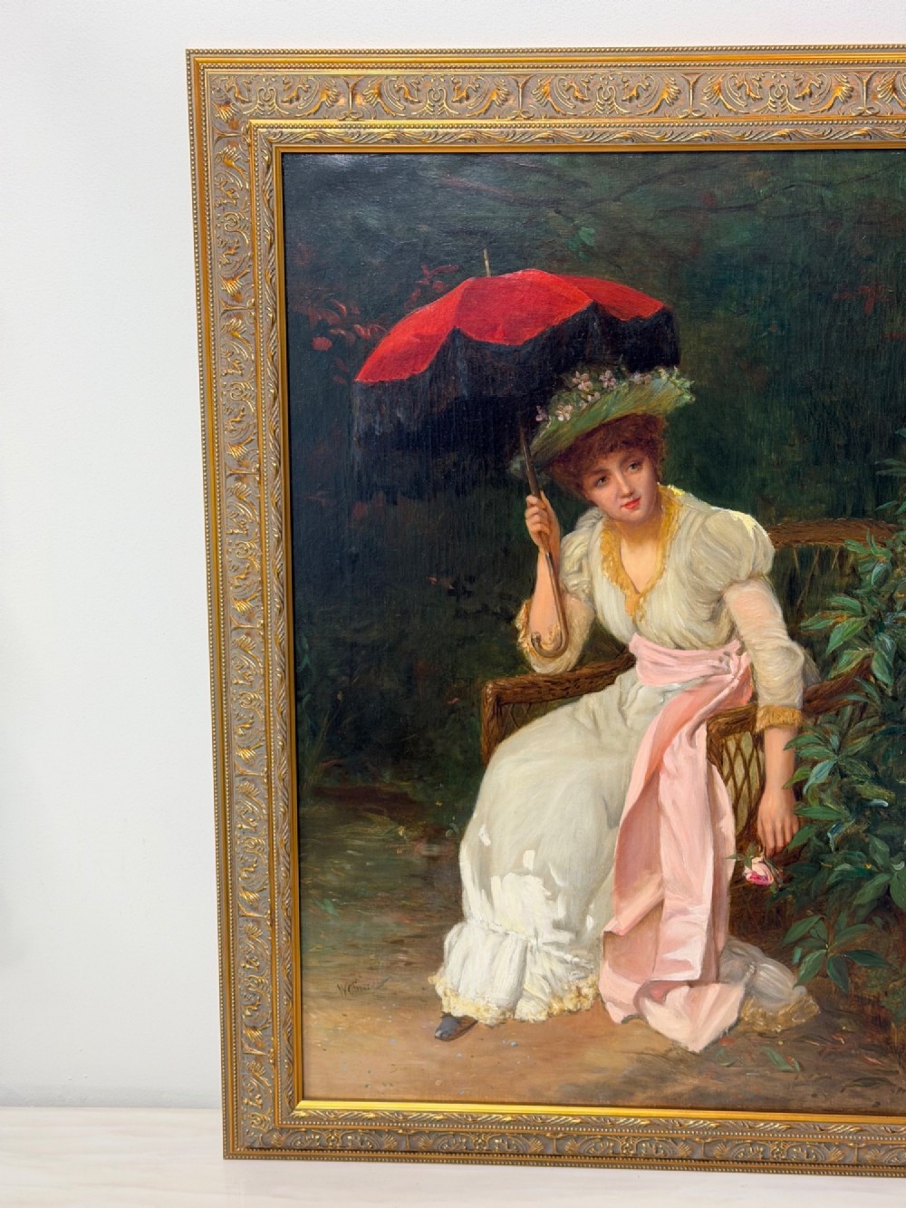 An antique oil painting depicting a seated woman in a white dress holding a red parasol, presented in an ornate carved gilded frame. View IV