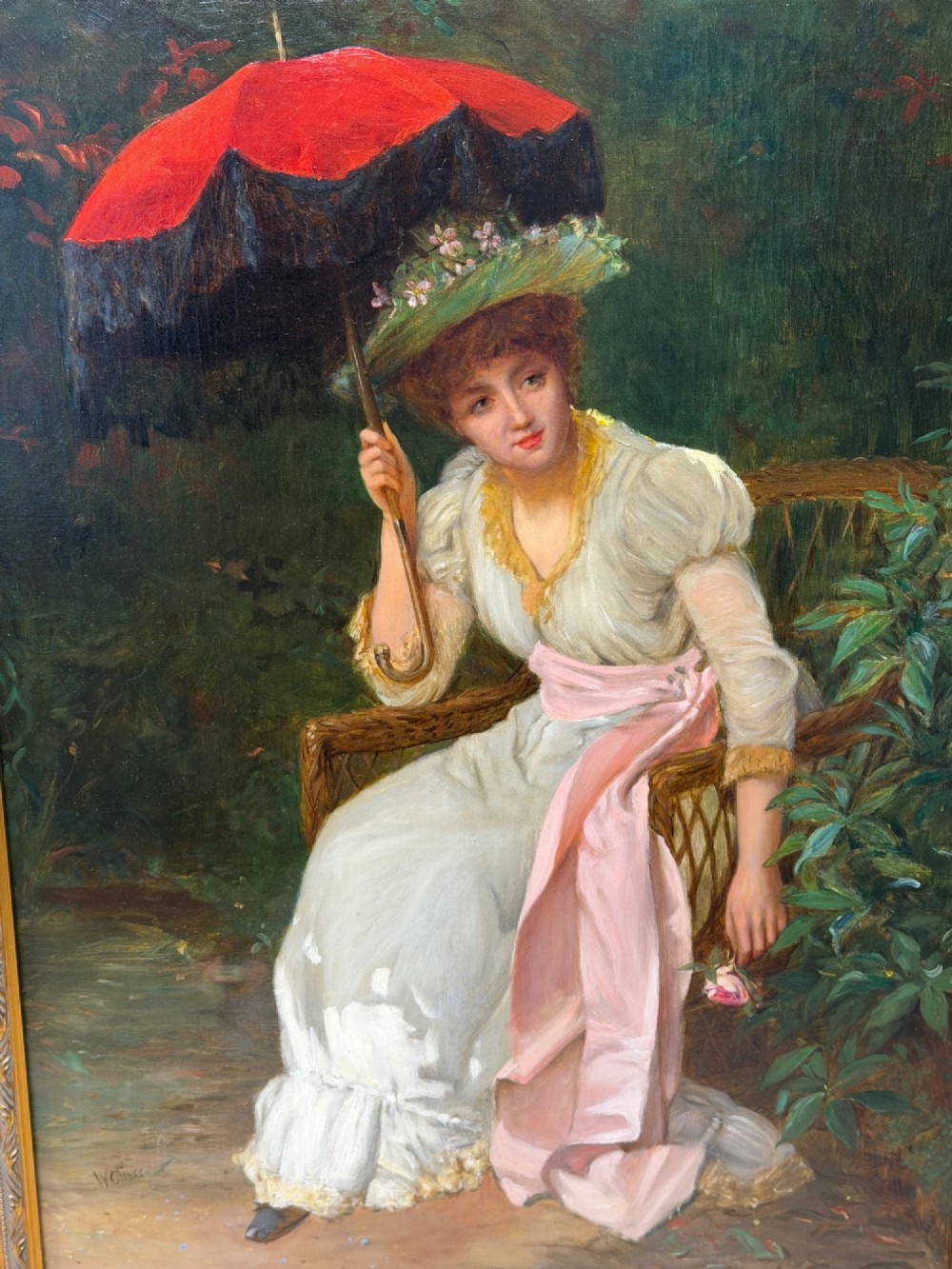 An antique oil painting depicting a seated woman in a white dress holding a red parasol, presented in an ornate carved gilded frame. View VII