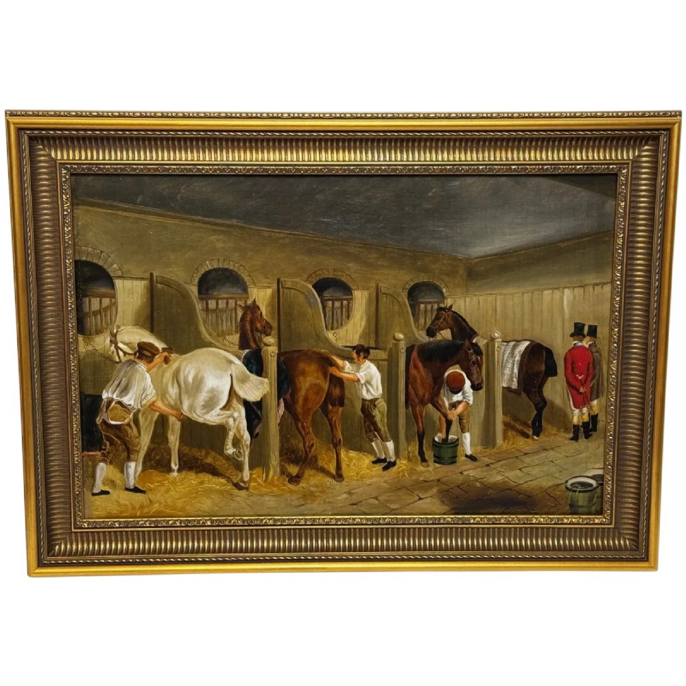 A horizontal oil painting depicting grooms tending to horses inside a stable block, housed within a fluted gilt wood frame.