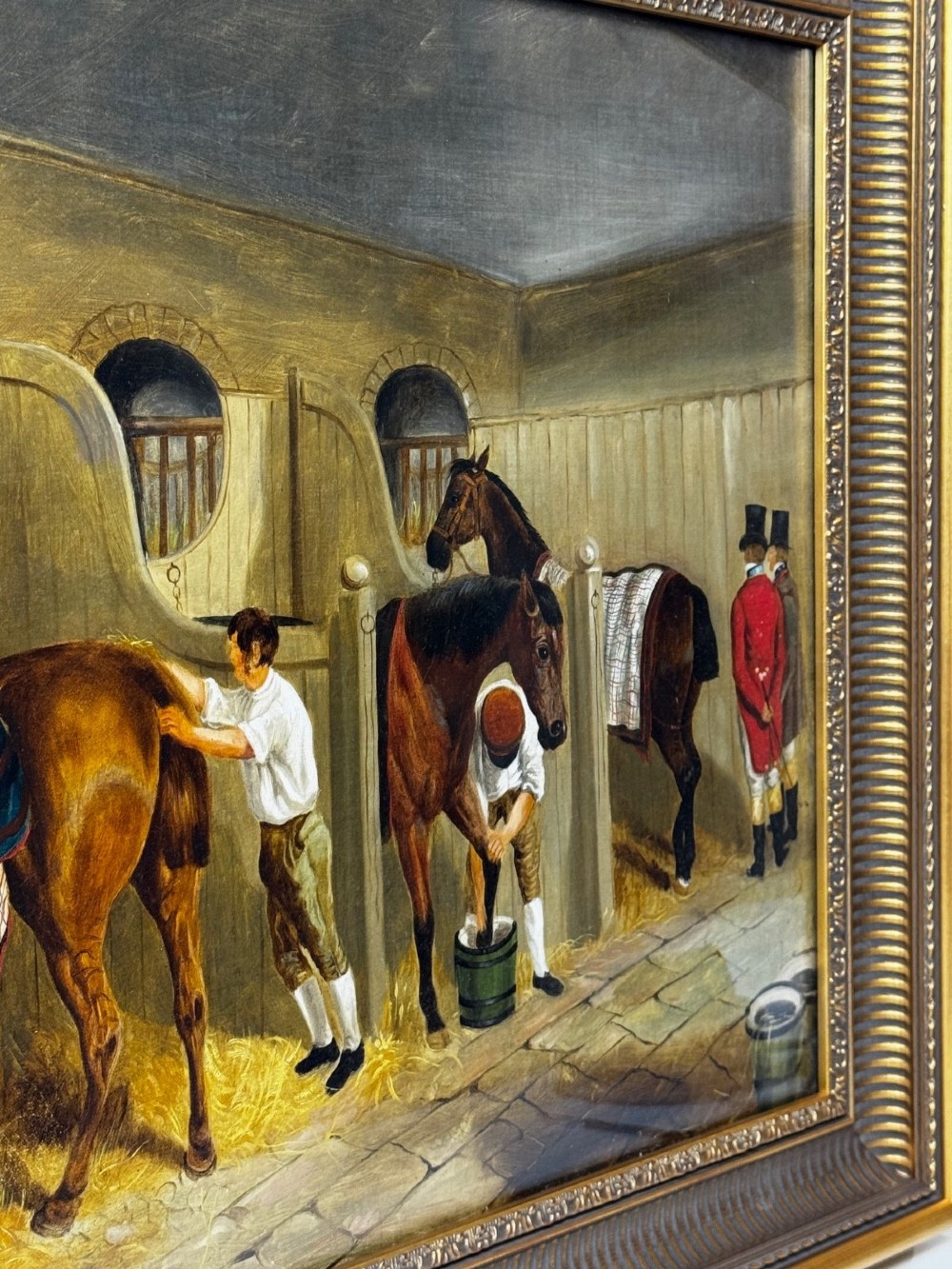 A horizontal oil painting depicting grooms tending to horses inside a stable block, housed within a fluted gilt wood frame. View II