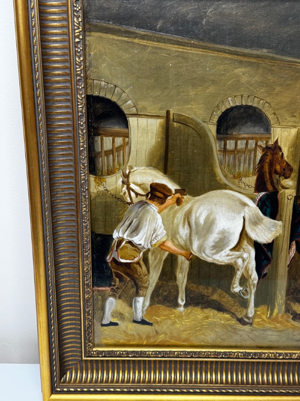 A horizontal oil painting depicting grooms tending to horses inside a stable block, housed within a fluted gilt wood frame. View VIII