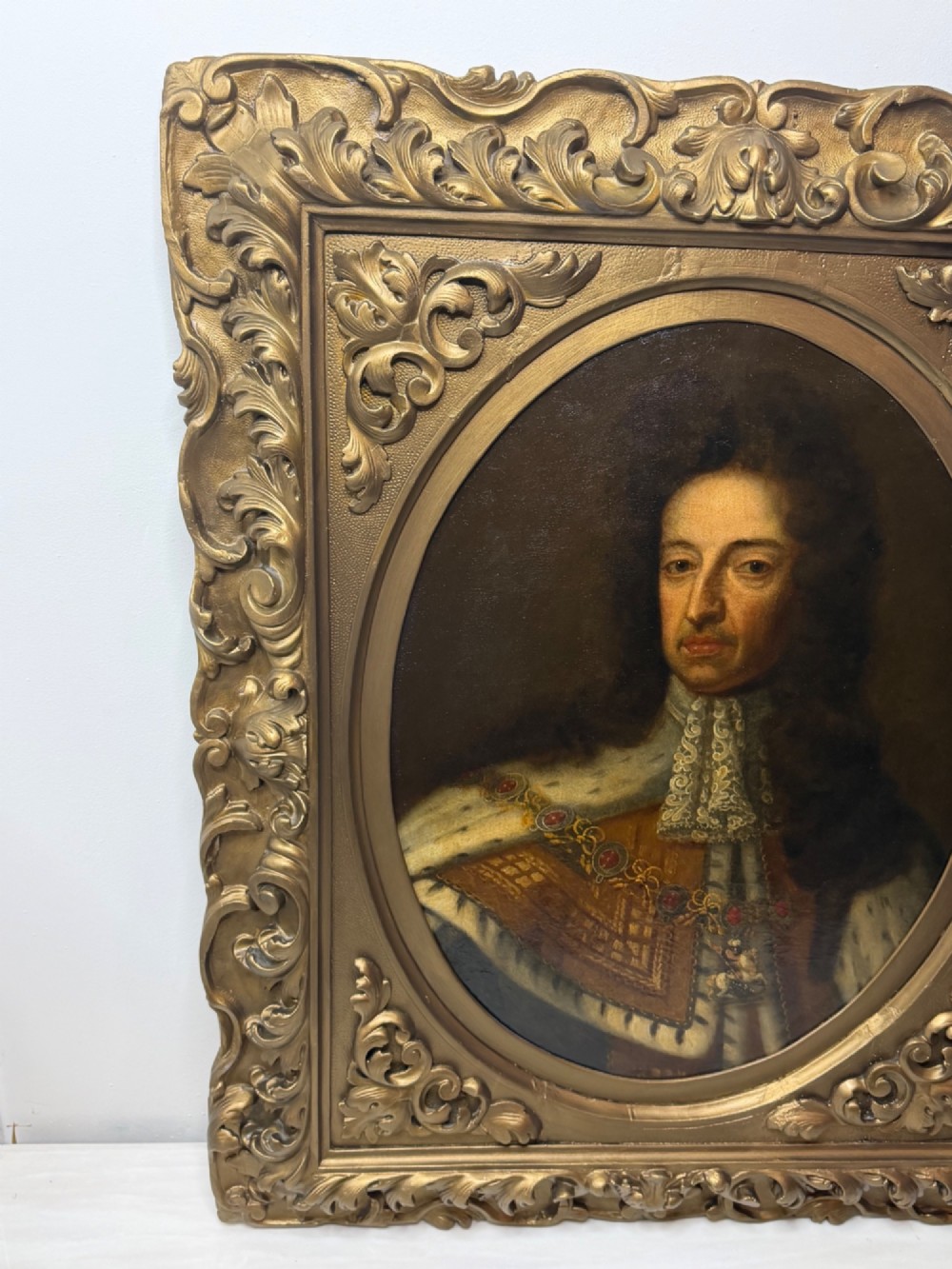 An 18th-century oil painting depicting King William III in a curled wig and ermine cloak, set within an oval aperture inside an ornate rectangular gold carved frame. View IV