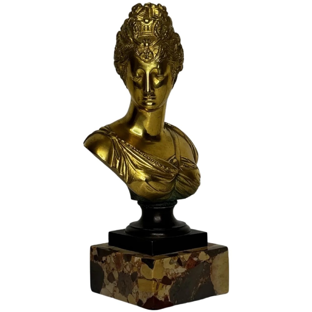 A 19th-century gilt bronze bust portrait of Diana de Poitiers featuring an ornate hairstyle and classical drapery, mounted on a dark socle and square variegated marble base.