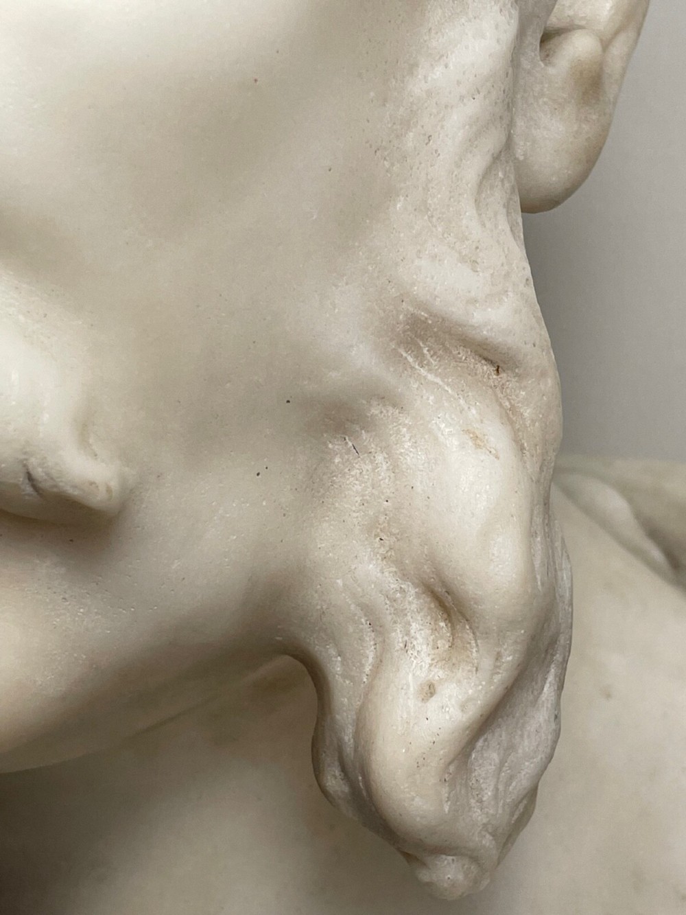 A carved off-white marble bust depicting a bald male figure with a prominent moustache wearing classical draped fabric across the shoulders. View II