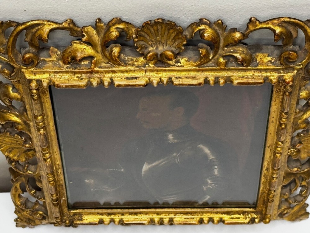 An antique profile portrait painting of a man wearing full steel armour, set within an ornate gilded frame decorated with carved shell and scroll motifs. View XIV
