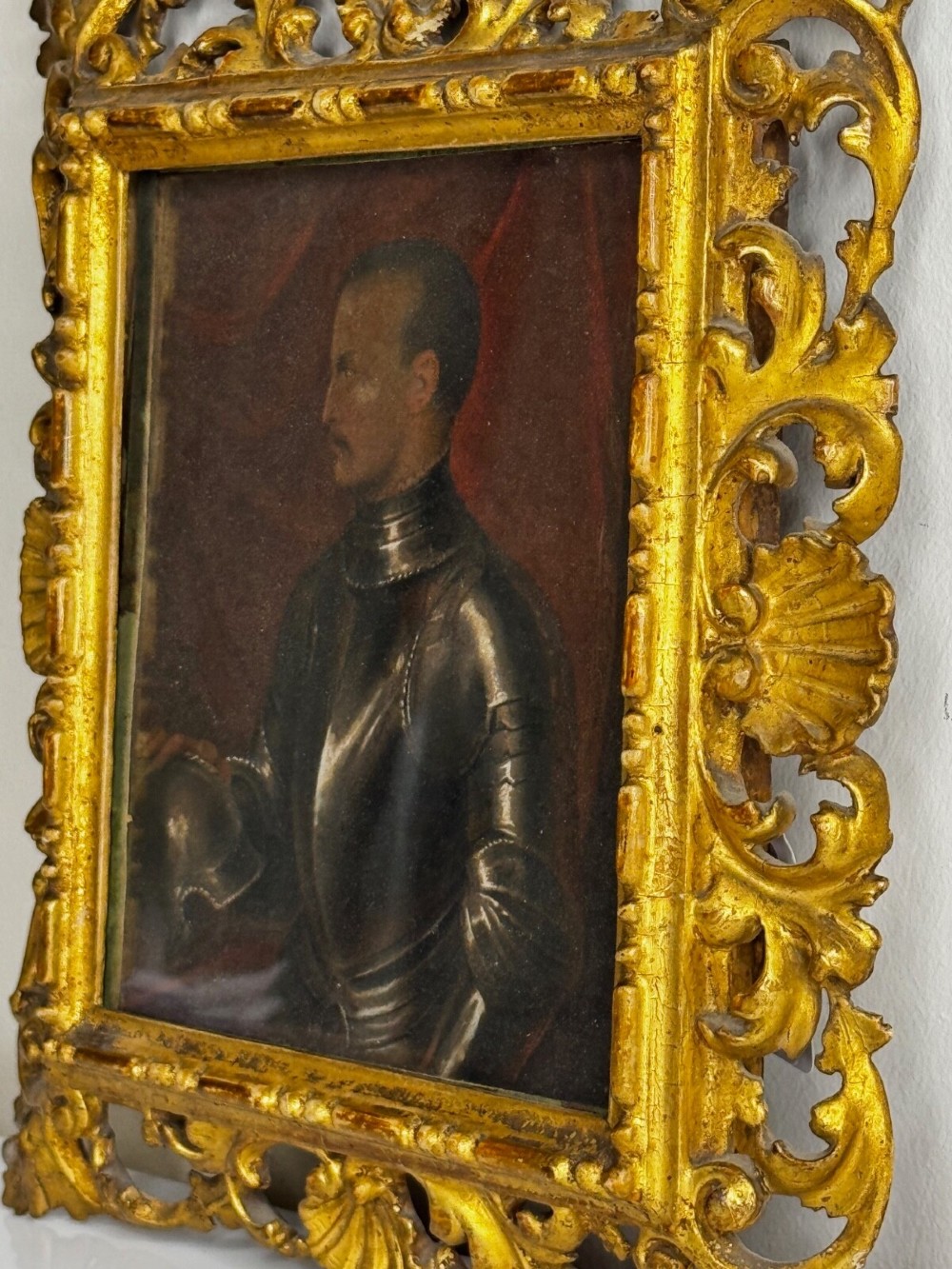 An antique profile portrait painting of a man wearing full steel armour, set within an ornate gilded frame decorated with carved shell and scroll motifs. View XV