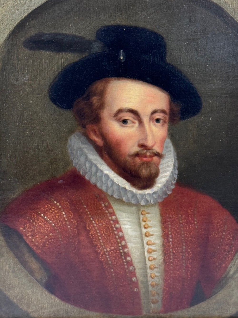 An 18th-century oil portrait of a man in a black hat, ruff collar, and crimson doublet set inside a carved gold-gilded frame. View III