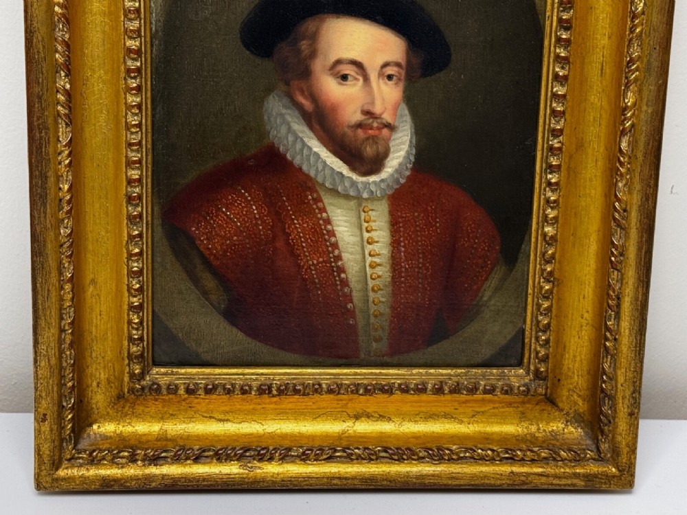 An 18th-century oil portrait of a man in a black hat, ruff collar, and crimson doublet set inside a carved gold-gilded frame. View XI