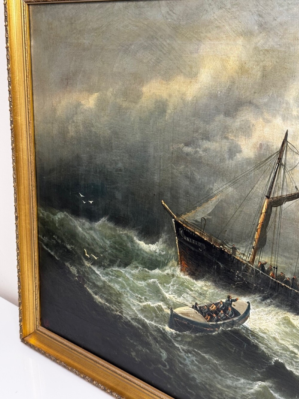 A late Victorian oil painting framed in gold depicting a steamship navigating turbulent dark green seas alongside a small rescue boat. View XII