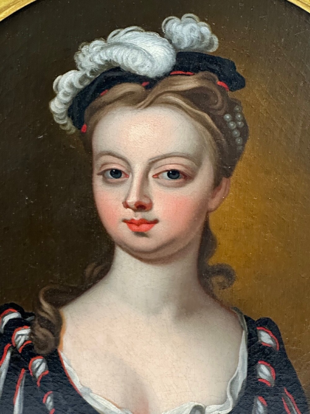 An early 18th-century oil portrait of a young woman wearing a dark gown with slashed sleeves, presented in a square giltwood frame with an oval spandrel. View II