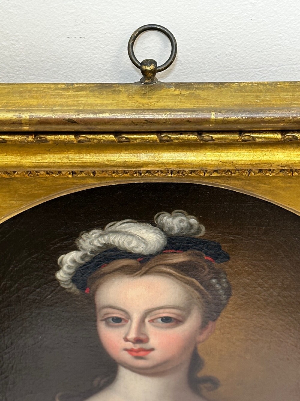 An early 18th-century oil portrait of a young woman wearing a dark gown with slashed sleeves, presented in a square giltwood frame with an oval spandrel. View VII