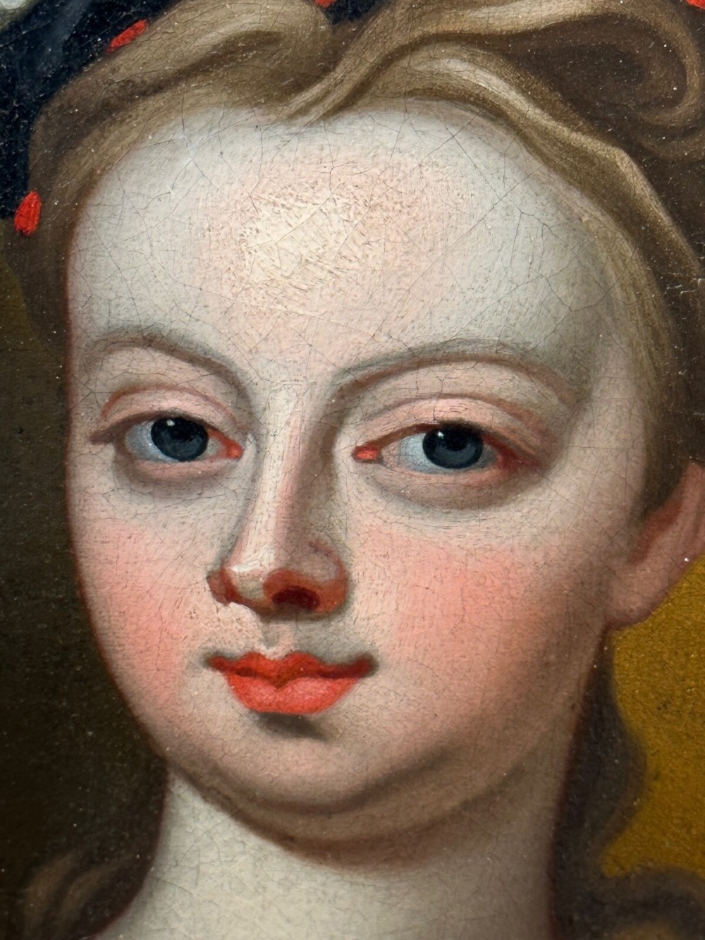 An early 18th-century oil portrait of a young woman wearing a dark gown with slashed sleeves, presented in a square giltwood frame with an oval spandrel. View VIII