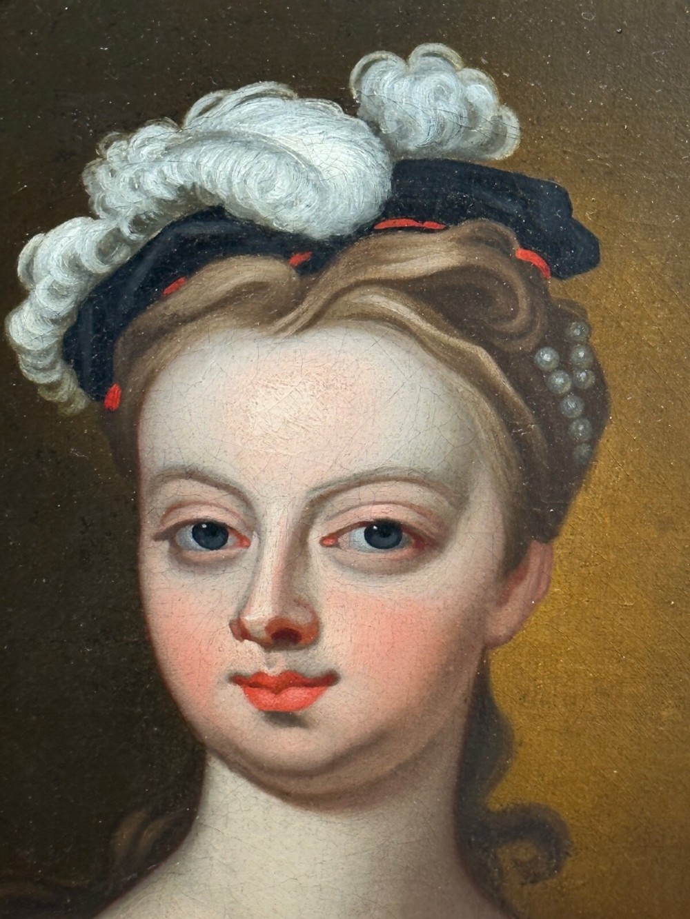 An early 18th-century oil portrait of a young woman wearing a dark gown with slashed sleeves, presented in a square giltwood frame with an oval spandrel. View XIV
