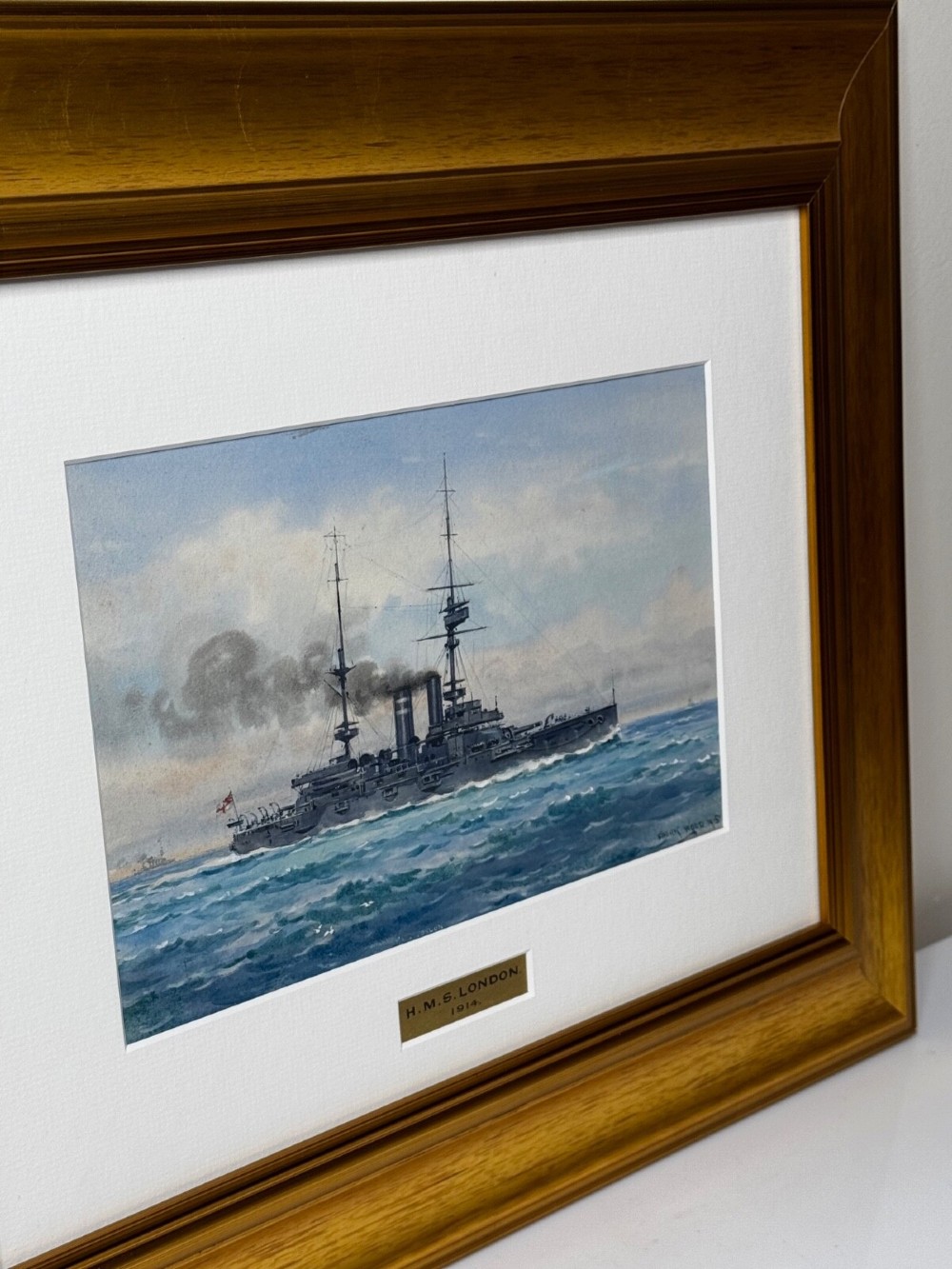 A framed watercolour painting depicting the WW1 battleship HMS London at sea, presented in a wide gold gilt frame with a white mount. View XIV
