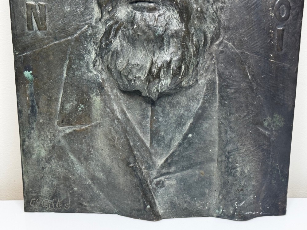 A rectangular dark bronze bas-relief plaque displaying a portrait of a bearded man with raised lettering and an incised signature. View V