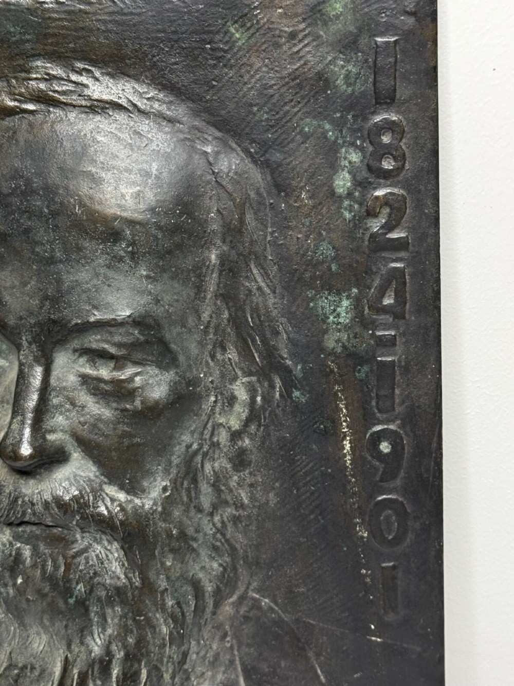 A rectangular dark bronze bas-relief plaque displaying a portrait of a bearded man with raised lettering and an incised signature. View IX