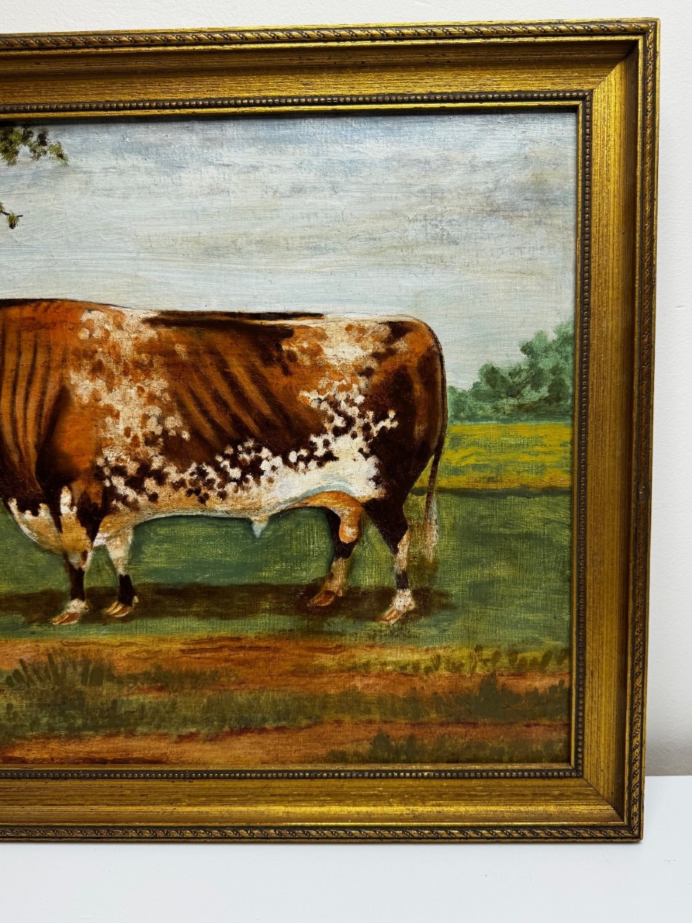 An antique Victorian oil painting depicting a brown and white shorthorn bull in a grassy field within a gilded frame. View III