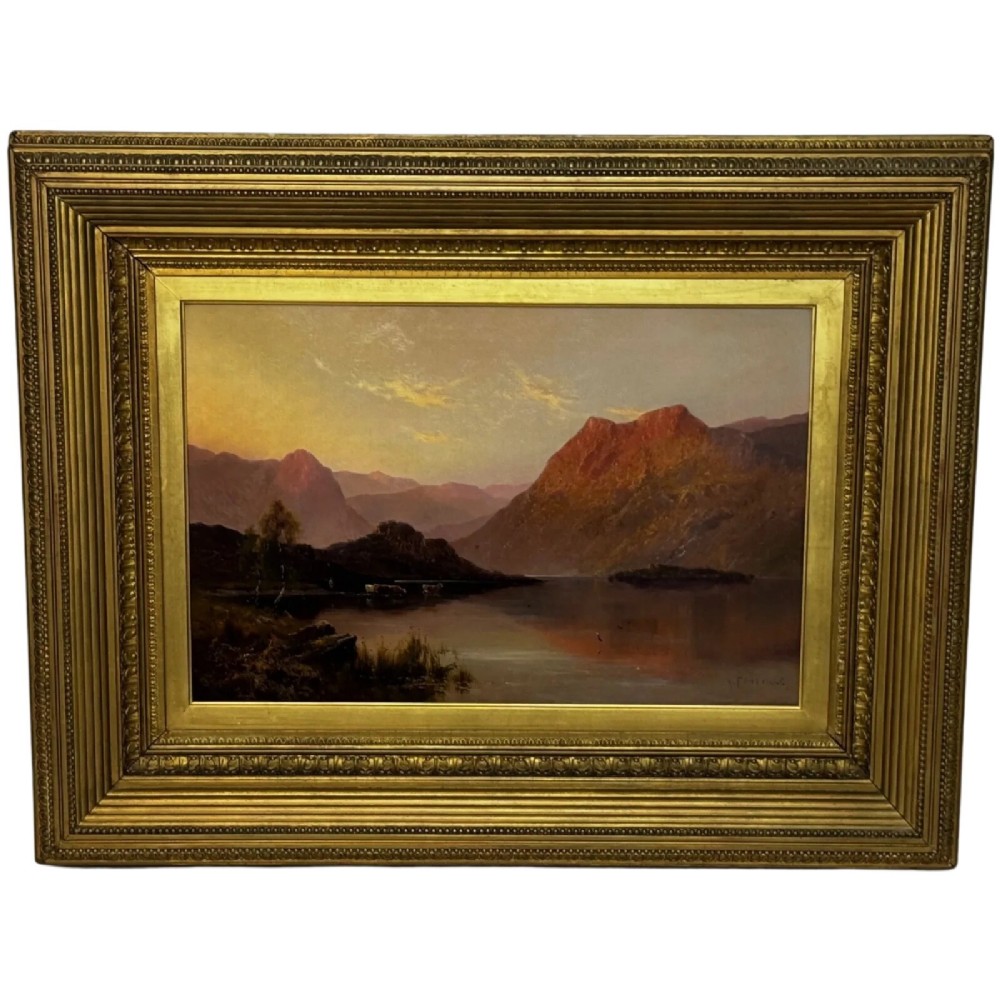 An antique oil painting depicting a lake surrounded by mountains at sunset, enclosed within a carved gold frame.
