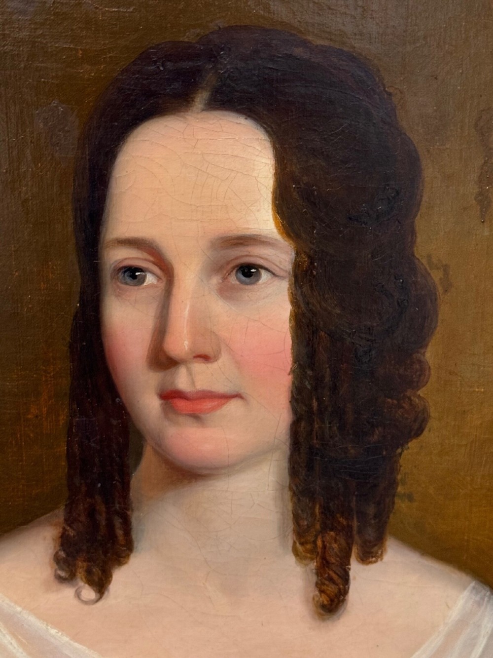 An antique oil painting depicting a woman in a white gown and red shawl set within a beaded giltwood frame. View II