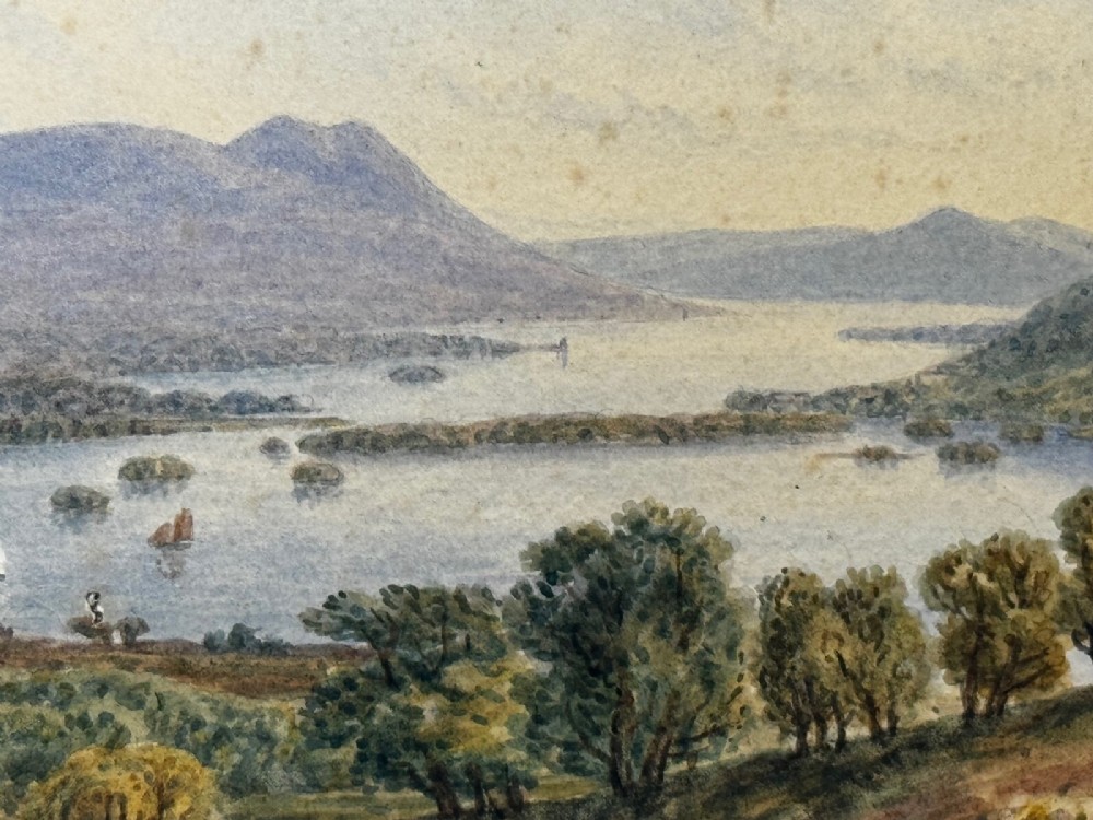 An antique Edwardian watercolour painting depicting Lake Windermere with distant hills, trees, and small boats, framed in gilt with a cream mount. View XI