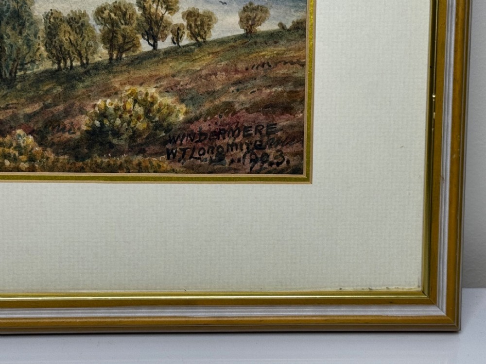 An antique Edwardian watercolour painting depicting Lake Windermere with distant hills, trees, and small boats, framed in gilt with a cream mount. View XII