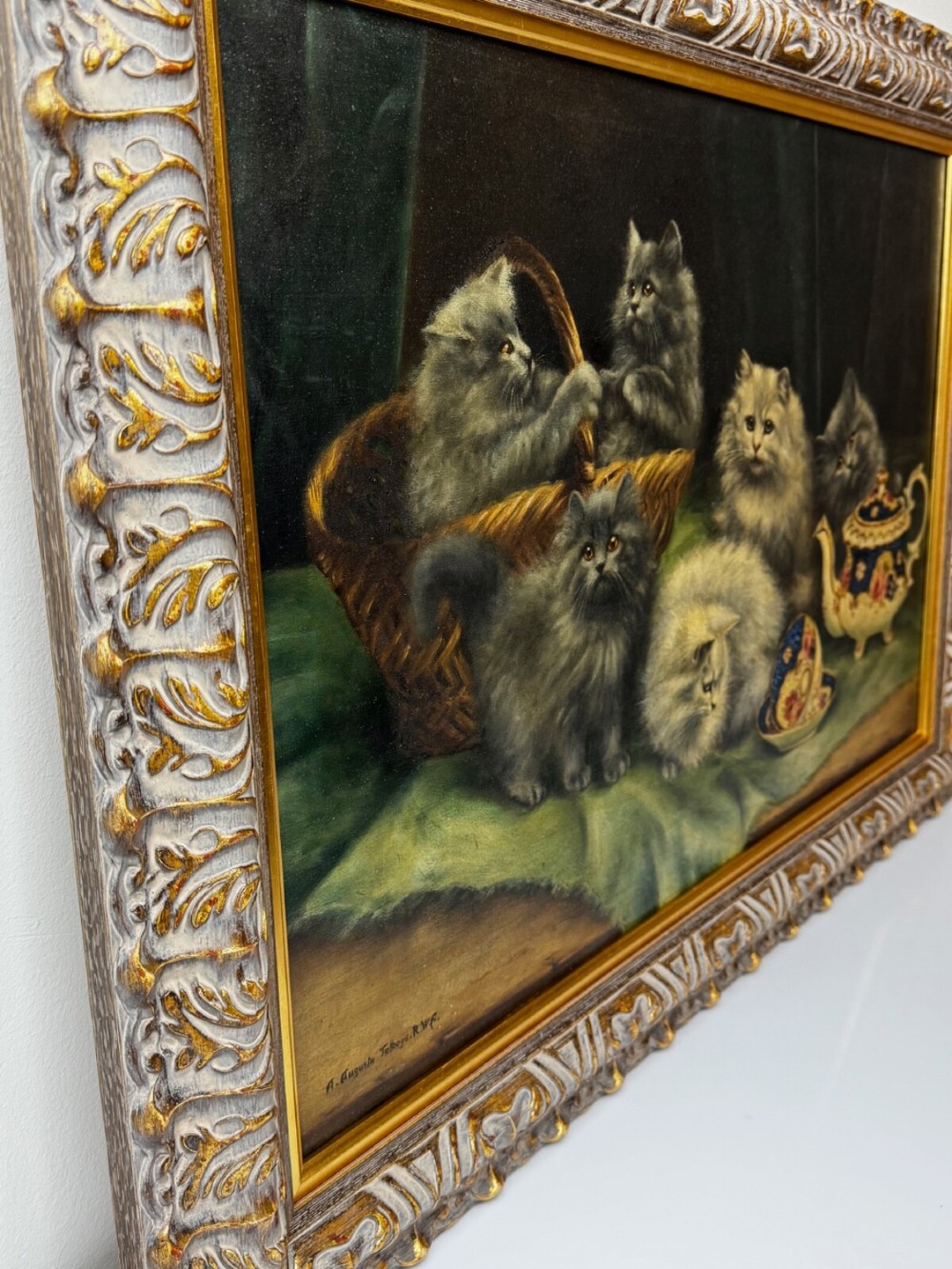 An antique framed oil painting depicting five grey and cream Persian kittens positioned around a wicker basket and a floral porcelain teapot. View IX