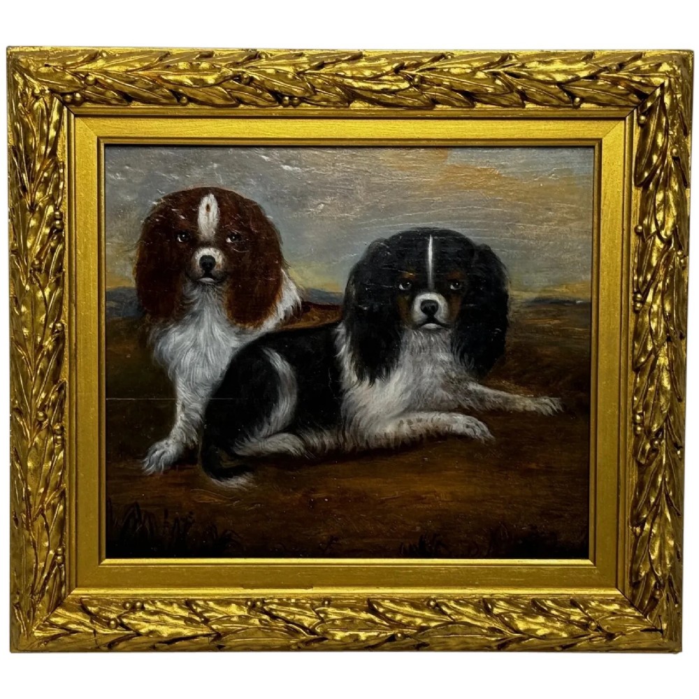 A nineteenth-century framed oil painting depicting a Blenheim spaniel and a tricolour spaniel seated outdoors, enclosed within an ornate gold giltwood frame.