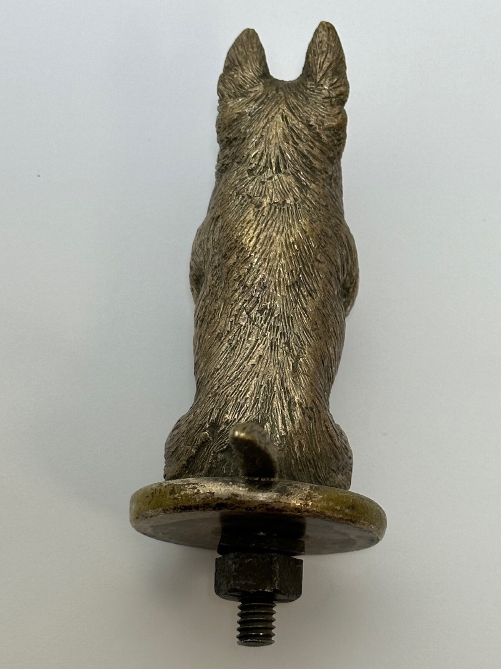 A cast bronze car mascot depicting a Scottish Terrier sitting in a begging pose mounted on a small circular base with a threaded bolt. View II