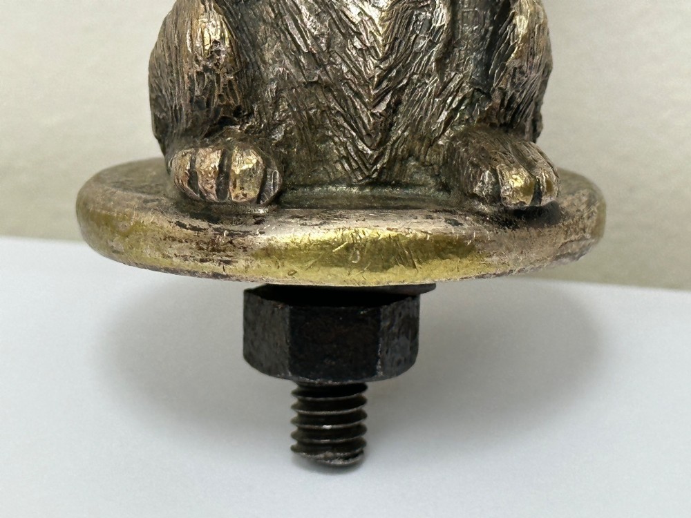 A cast bronze car mascot depicting a Scottish Terrier sitting in a begging pose mounted on a small circular base with a threaded bolt. View IV