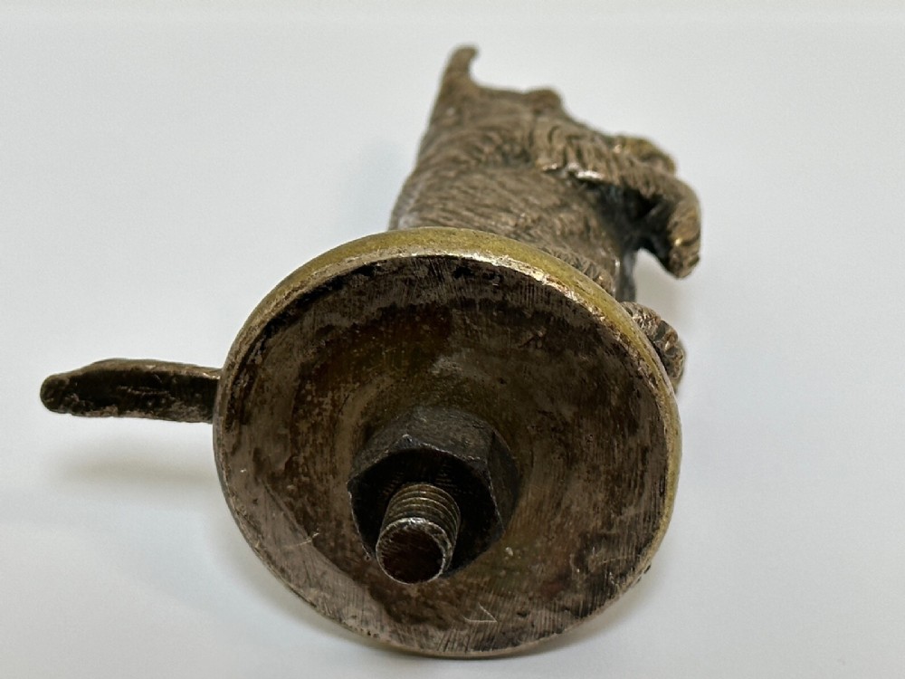 A cast bronze car mascot depicting a Scottish Terrier sitting in a begging pose mounted on a small circular base with a threaded bolt. View VI
