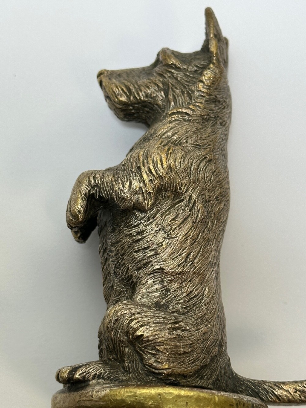 A cast bronze car mascot depicting a Scottish Terrier sitting in a begging pose mounted on a small circular base with a threaded bolt. View VIII