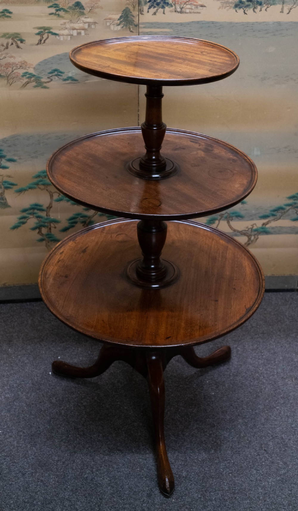 A George III mahogany three-tier dumb waiter featuring graduated circular trays supported by a central turned column and a pad-footed tripod base.