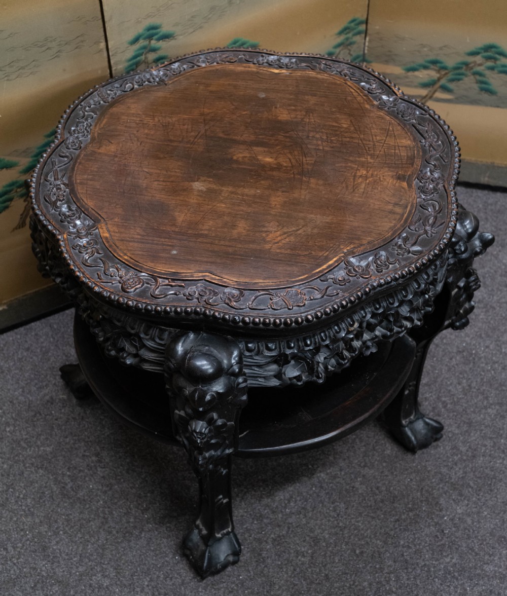 A dark rosewood Chinese occasional table featuring a lobed inset top, deeply carved floral aprons, curved legs, and a lower tier shelf. View II