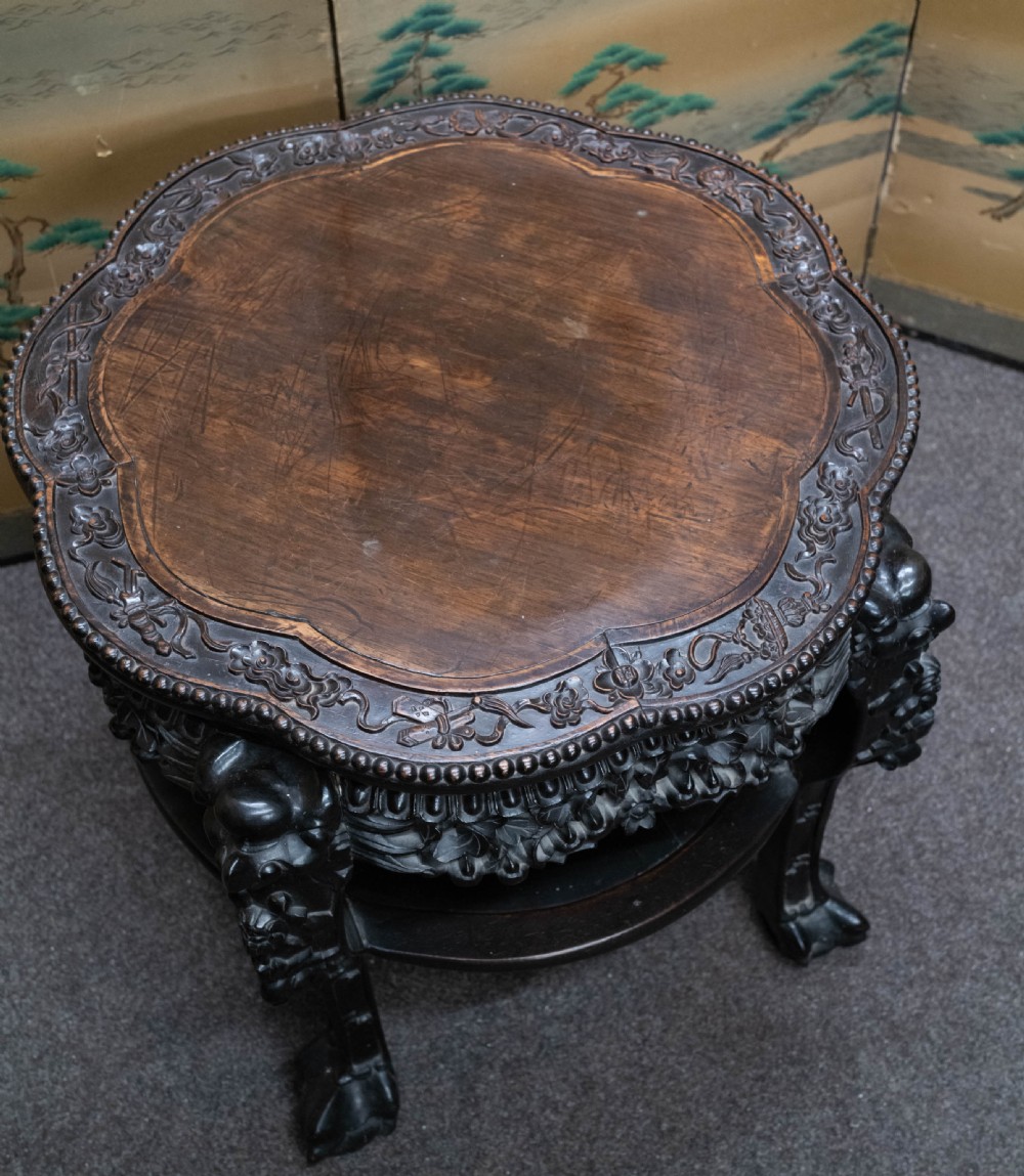 A dark rosewood Chinese occasional table featuring a lobed inset top, deeply carved floral aprons, curved legs, and a lower tier shelf. View V