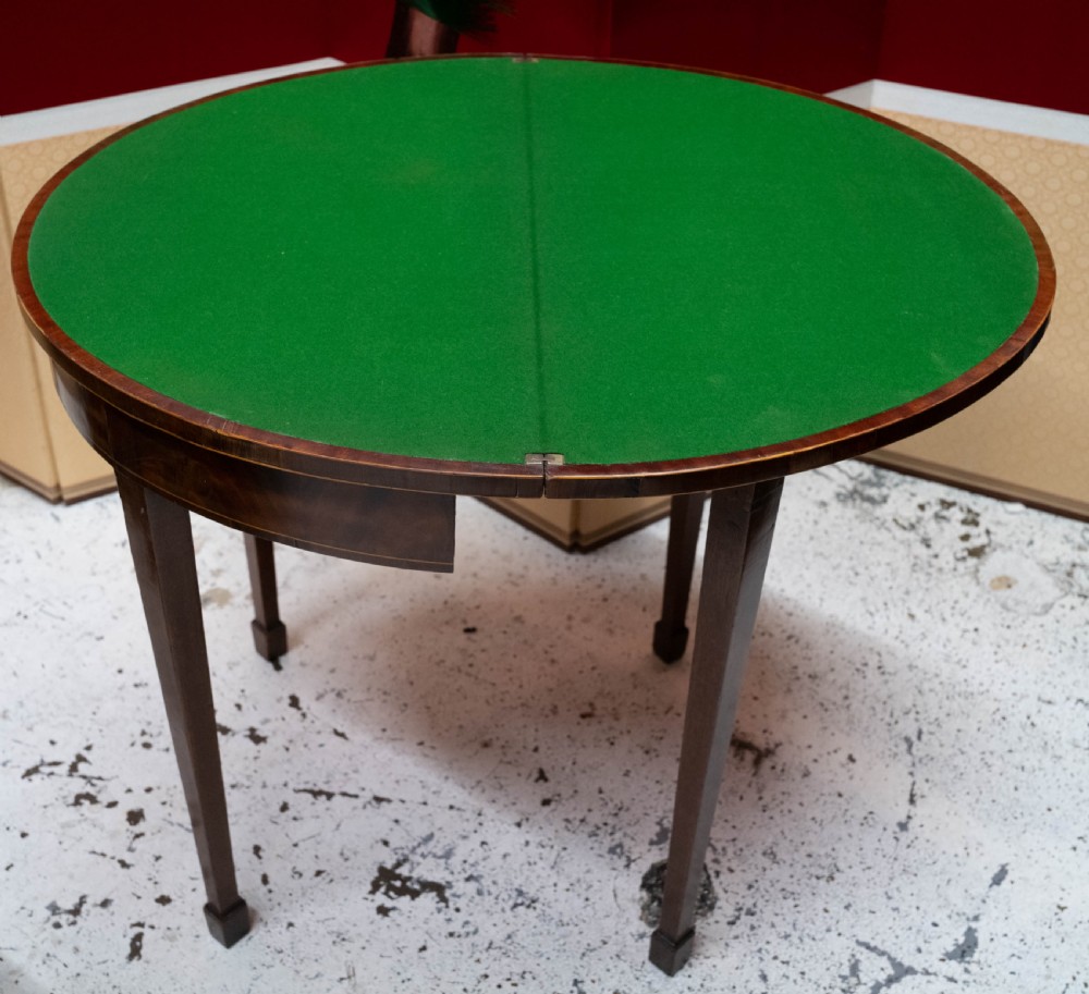A George III circular mahogany card table with a green baize playing surface and rosewood crossbanding on tapered legs.