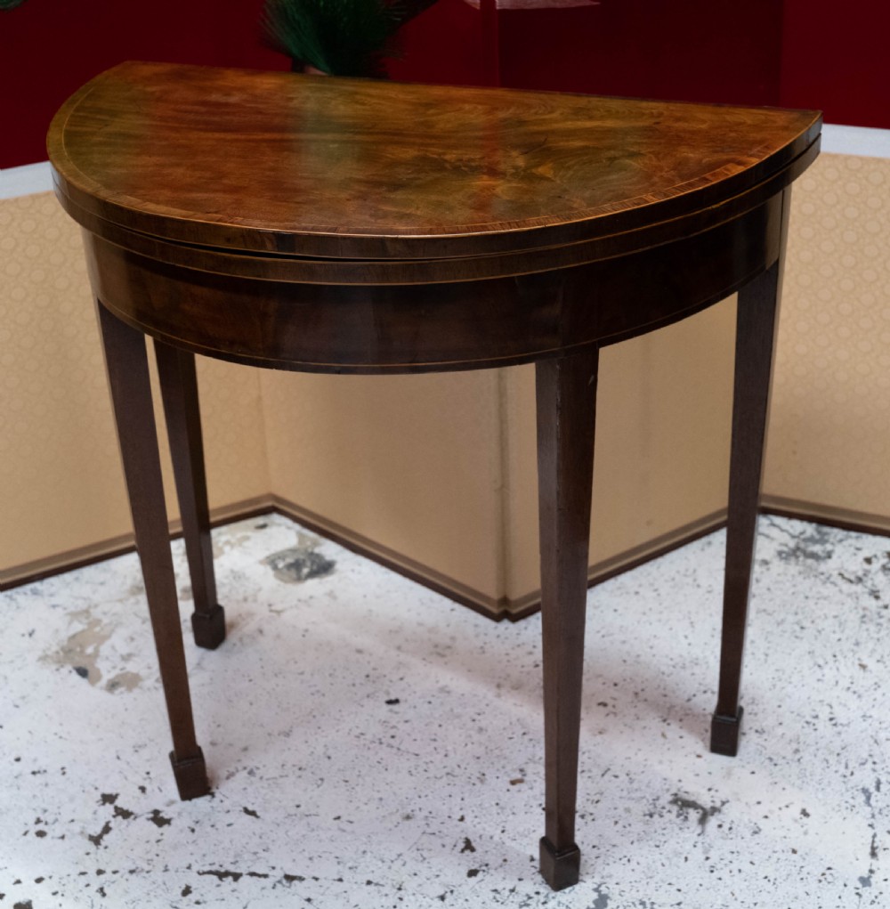 A George III circular mahogany card table with a green baize playing surface and rosewood crossbanding on tapered legs. View II