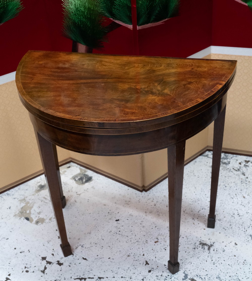 A George III circular mahogany card table with a green baize playing surface and rosewood crossbanding on tapered legs. View III