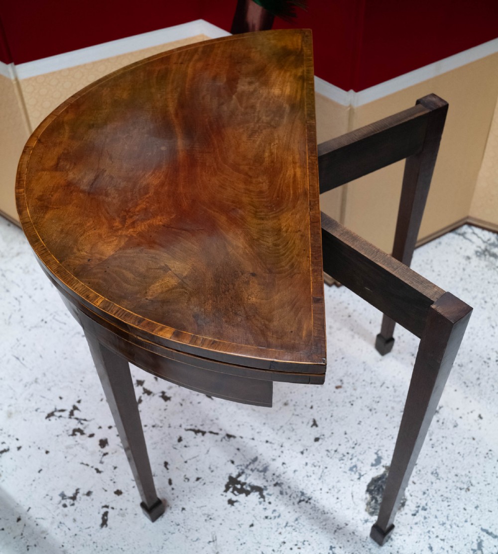 A George III circular mahogany card table with a green baize playing surface and rosewood crossbanding on tapered legs. View V