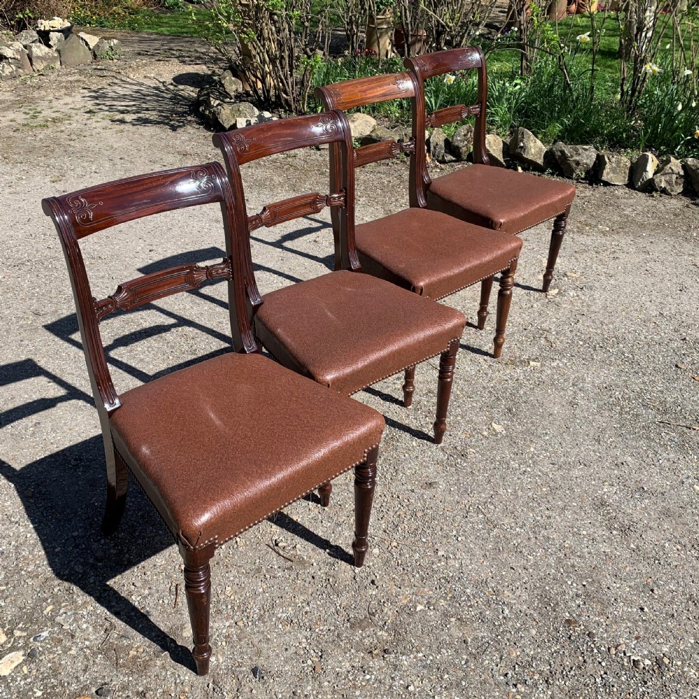 A set of four Regency mahogany dining chairs with carved bar backs, dark brown upholstered seats, and turned front legs.