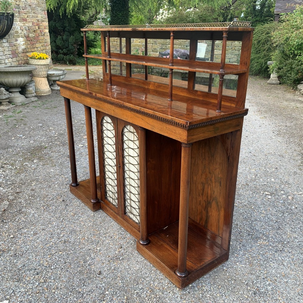 A Regency rosewood breakfront chiffonier cabinet featuring an upper mirrored shelf unit supported by turned columns over central mesh-panelled doors lined with fabric. View II