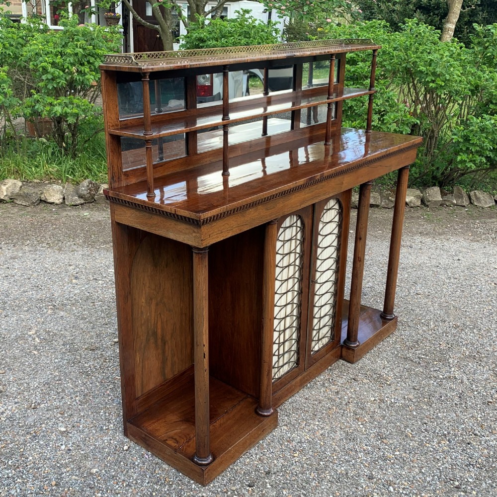 A Regency rosewood breakfront chiffonier cabinet featuring an upper mirrored shelf unit supported by turned columns over central mesh-panelled doors lined with fabric. View III
