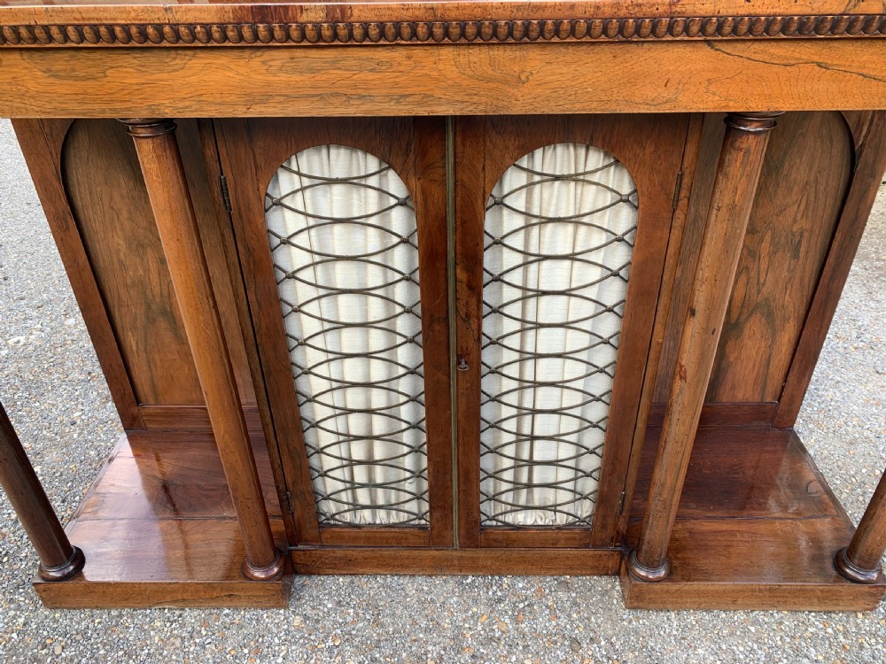 A Regency rosewood breakfront chiffonier cabinet featuring an upper mirrored shelf unit supported by turned columns over central mesh-panelled doors lined with fabric. View V