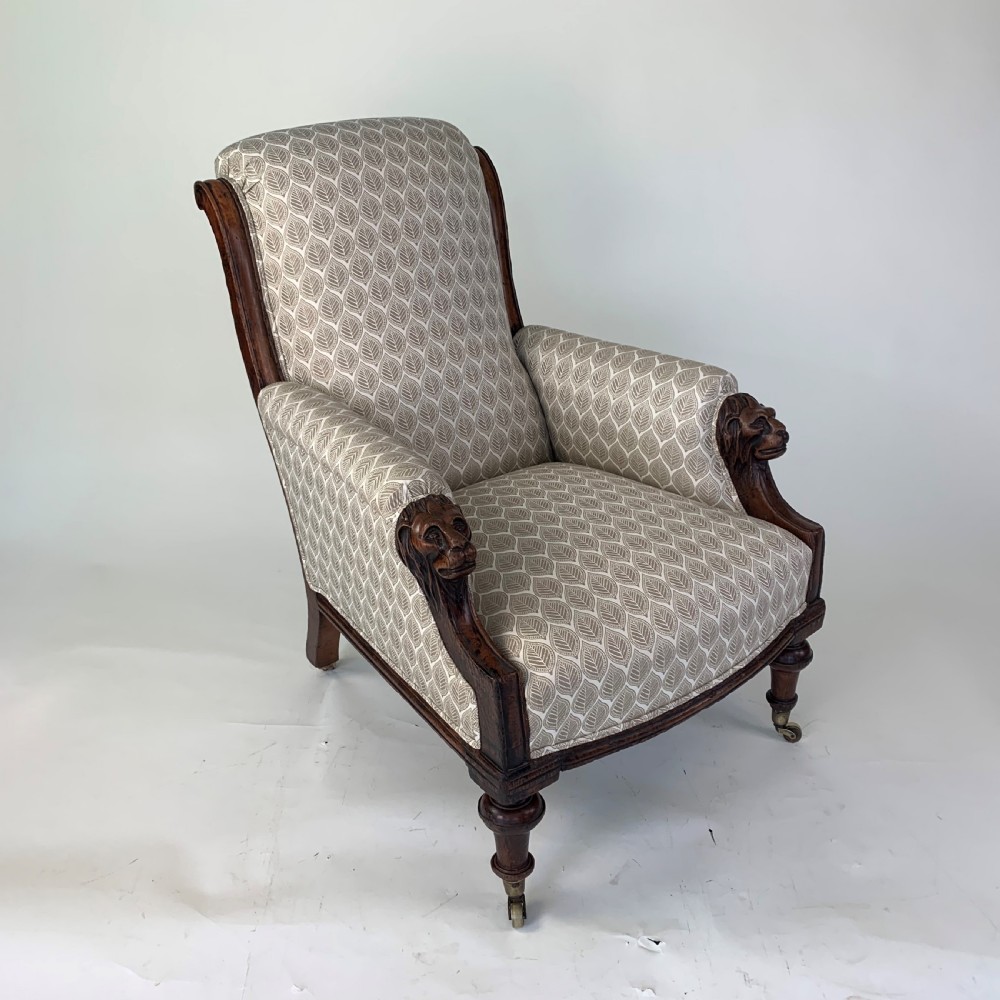 An antique high-back armchair featuring carved lion head armrests, turned wooden legs on castors, and patterned fabric upholstery.